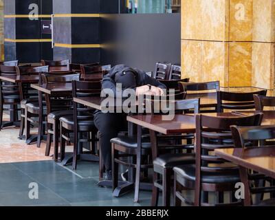 SINGAPORE – 12 MAR 2020 – A woman wearing a hijab takes a nap at the empty tables of the closed Hard Rock Cafe restaurant on Sentosa Island, Singapore Stock Photo