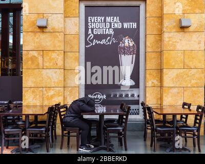 SINGAPORE – 12 MAR 2020 – A woman wearing a hijab takes a nap at the empty tables of the closed Hard Rock Cafe restaurant on Sentosa Island, Singapore Stock Photo