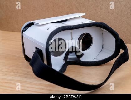 A cardboard VR headset. View from the back, the strap and lenses are visible. Resting on a wooden table next to a cork wall. Stock Photo