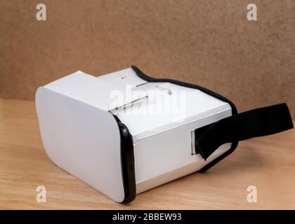 A cardboard VR headset. View from an angle at the front. The front is closed and the edge of the mobile phone inserted in it is visible. It is on a wo Stock Photo