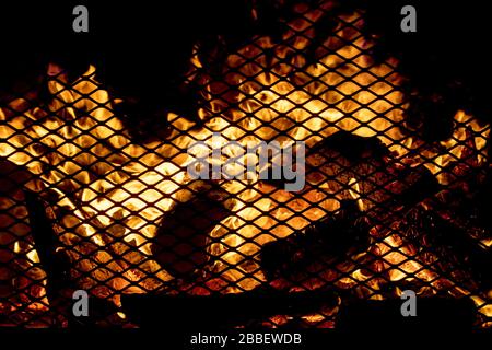 An outdoor fire in a heavy screen fireplace at night. Scene is dark except for the flames. Focus is on the burning wood embers. Stock Photo