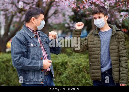 father and son with a face mask shake hands in the city outdoor, blooming trees, spring season, flowering time - concept of allergies and health prote Stock Photo