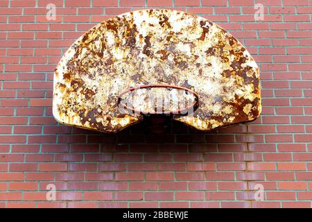 An old basketball hoop mounted outdoors on a brick wall. The netting is gone, and the backboard is dirty and rusty. Room for text. Stock Photo