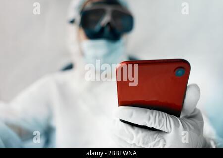 Virologist person protects himself from a global pandemic and holds a phone in his hands. Stock Photo