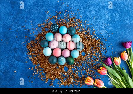 Colorful Easter eggs on golden decorative rocks and tulips. Dark blue background. Holiday decorations, Easter concept background. Stock Photo