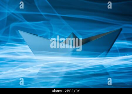Paper boat splitting blue light trails symbolizing waves in the sea Stock Photo