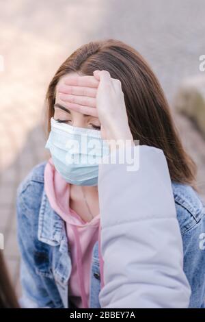 Woman in mask. Coronavirus theme. Women in the city measures temperature with a hand Stock Photo