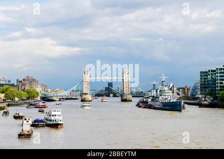 The Tower Bridge opens for a cruise boat in London, England.  The HMS Belfast is on the right. Stock Photo