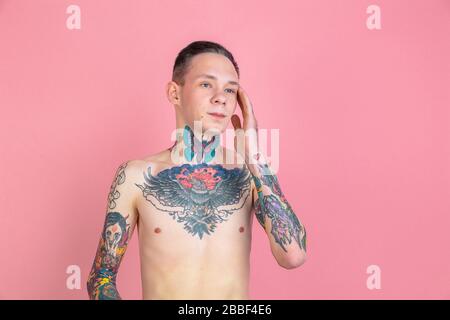 Thinking. Portrait of young man with freaky appearance on pink background. Unusual look with huge tattooes. Doing daily routine. Human emotions, facial expression, sales, ad concept. Youth culture. Stock Photo