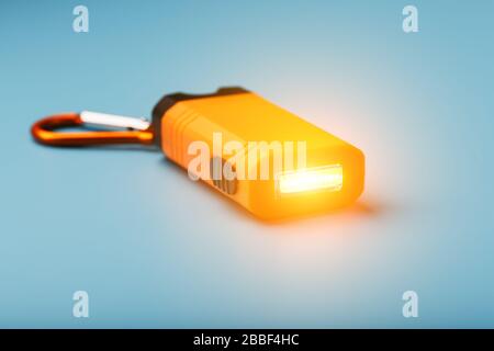 Orange led Flashlight with a carabiner on a blue background. LED lights in flight. Stock Photo