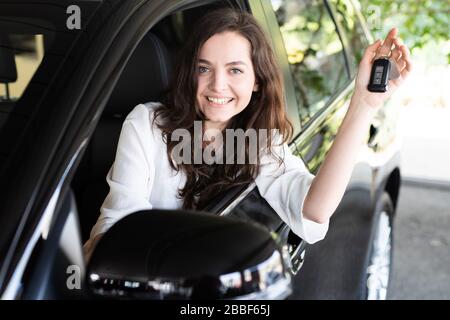 Attractive young woman laughing happily in a car in a car dealership and holding the car key Stock Photo