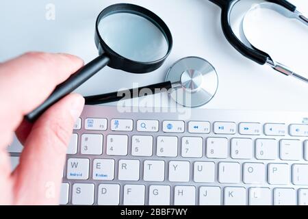 Medical stethoscope and magnifying glass on laptop keyboard. Blue Background Stock Photo