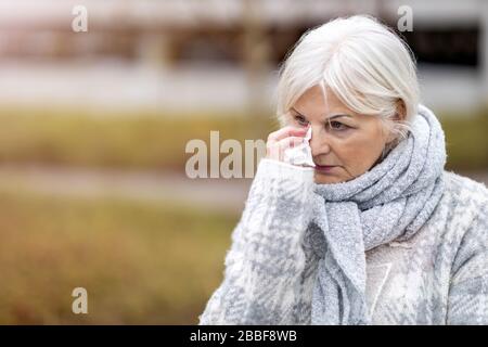 Unhappy senior woman wipes her eyes with a tissue Stock Photo