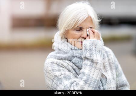 Unhappy senior woman wipes her eyes with a tissue Stock Photo
