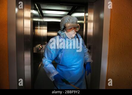 Coronavirus infection. Paramedic in protective mask and costume disinfecting an elevator with sprayer Stock Photo