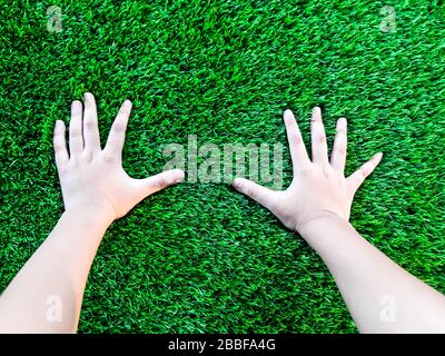 Artificial grass background. a Hand of a child on a green artificial turf floor. the child play is fun. Stock Photo