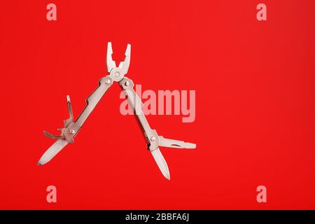 Multitool is a multi-functional tool on a red background. The concept of an open, flying multi-tool with free space. Stock Photo