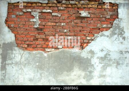 Gray concrete wall with half-peeled plaster from which uneven masonry of red brick is visible, taken from the front, background Stock Photo