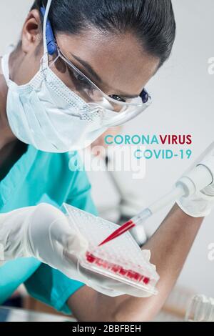 Female Asian Indian medical scientist researcher or doctor wearing a face mask testing Coronavirus COVID-19 blood sample in a laboratory with her coll Stock Photo