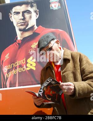 A Liverpool fan reads the match day programme beside a large poster of club captain Steven Gerrard Stock Photo