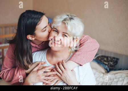 Young daughter of mature beautiful blonde mother kissing Stock Photo