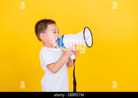 Asian Thai happy portrait cute little cheerful child boy holding and shouting or screaming through the megaphone her looking to side, studio shot isol