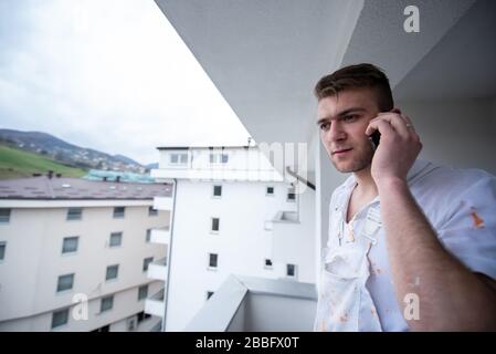 Painter making telephone call while standing on balcony during break from work  Decorator Using Mobile Phone Standing Outside Stock Photo