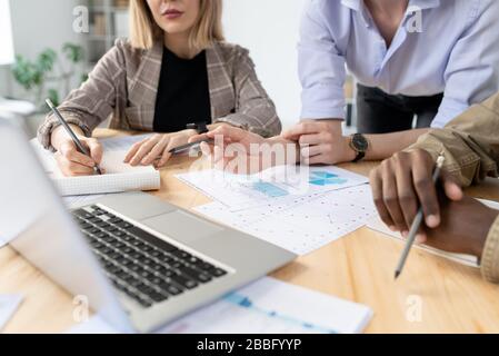 Close-up of business experts watching presentation on laptop while analyzing graphs and charts at meeting Stock Photo