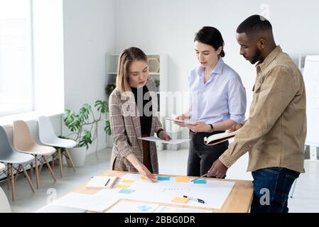 Busy young interracial colleagues discussing creative ideas for startup project while making task board Stock Photo