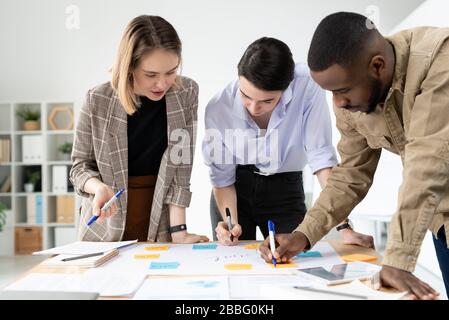 Multi-ethnic marketing specialists standing around table and adding new ideas on creative plan board Stock Photo