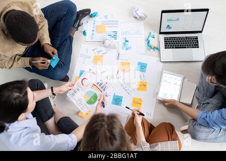 Directly above view of multi-ethnic colleagues sitting on floor with papers and devices and discussing project tasks Stock Photo