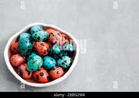 Painted red and blue quail eggs for Easter in small ceramic plate on gray concrete background. Empty place for text and sign. Stock Photo