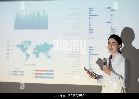 Content female medical student in lab coat using tablet while giving speech on coronavirus infection at conference Stock Photo