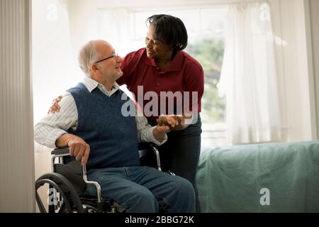 Smiling female nurse comforting an elderly male patient in a wheelchair. Stock Photo