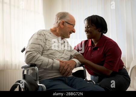 Smiling female nurse comforting an elderly male patient in a wheelchair. Stock Photo