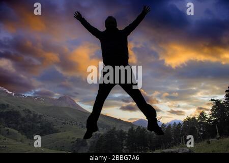 Man is jumping from a stone while the sun is setting. Magnificent clouds upon the world. Young man trying to do X figure with his arms and legs. Stock Photo