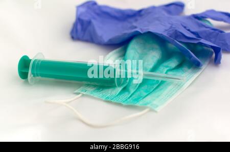 Used green disposable face mask, blue latex glove and plastic syringe Stock Photo