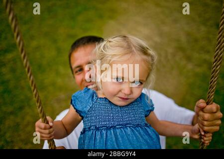 Portrait of a young girl playing on a rope swing with her father Stock Photo