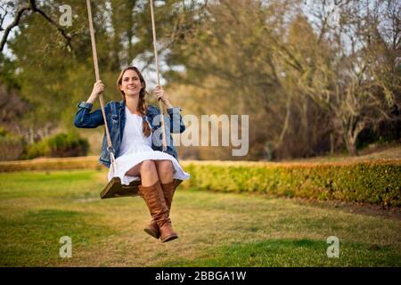 Happy young woman swinging on a wooden rope swing Stock Photo