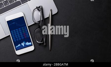 Office workplace table with supplies, laptop and smartphone with stock market data and chart. Flat lay. Top view with space for your text Stock Photo