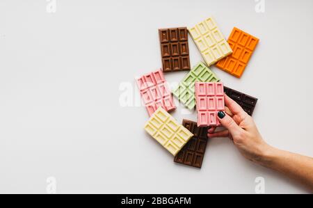 Woman with bright manicure holds in his hand chocolate of various colors and colored fillings with slices of fruit nuts Stock Photo