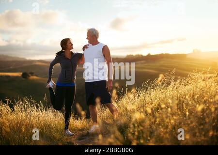Senior man and young woman stretching before running on outdoor trail Stock Photo