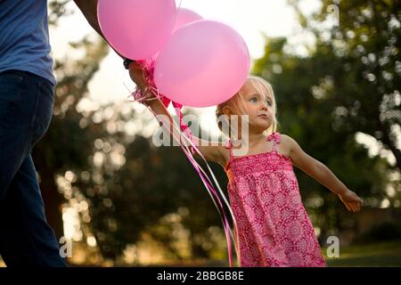 Young girl with pink balloons holding her father's hand Stock Photo