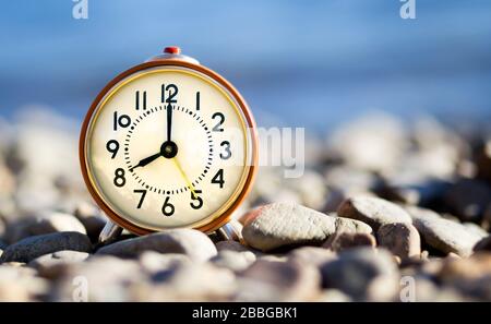 Daylight savings time concept, retro alarm clock standing on the beach Stock Photo