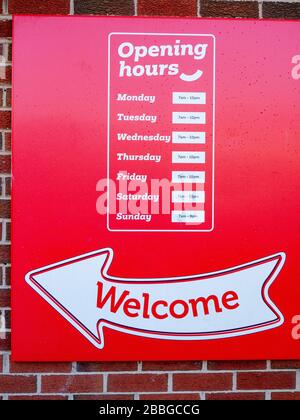 Red Welcome Opening hours sign on outside wall UK Stock Photo