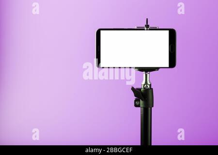 Mobile phone on a tripod with a clear white display for images and text, pink isolated background. Stock Photo