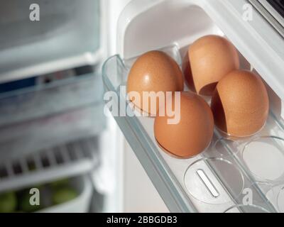 Four fresh chicken eggs on shelf of white refrigerator. Stock Photo