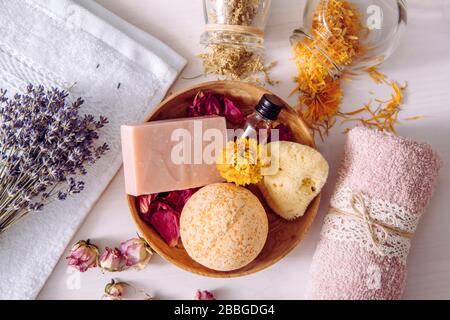 Various organic dried herbs flower petals used in beauty bath products concept. Top view of bath bomb, natural sea sponge, bar of soap, aroma oil. Stock Photo