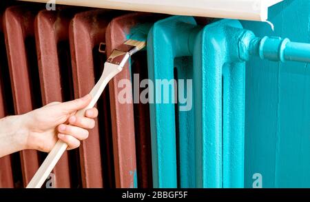 Home refreshing renovation concept. Close up view of man hand painting with special curved radiator paint brush. Stock Photo