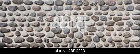 Pebble stone wall texture background. Cement plaster wall decorated by large natural pebble stones. Building facade decoration Stock Photo